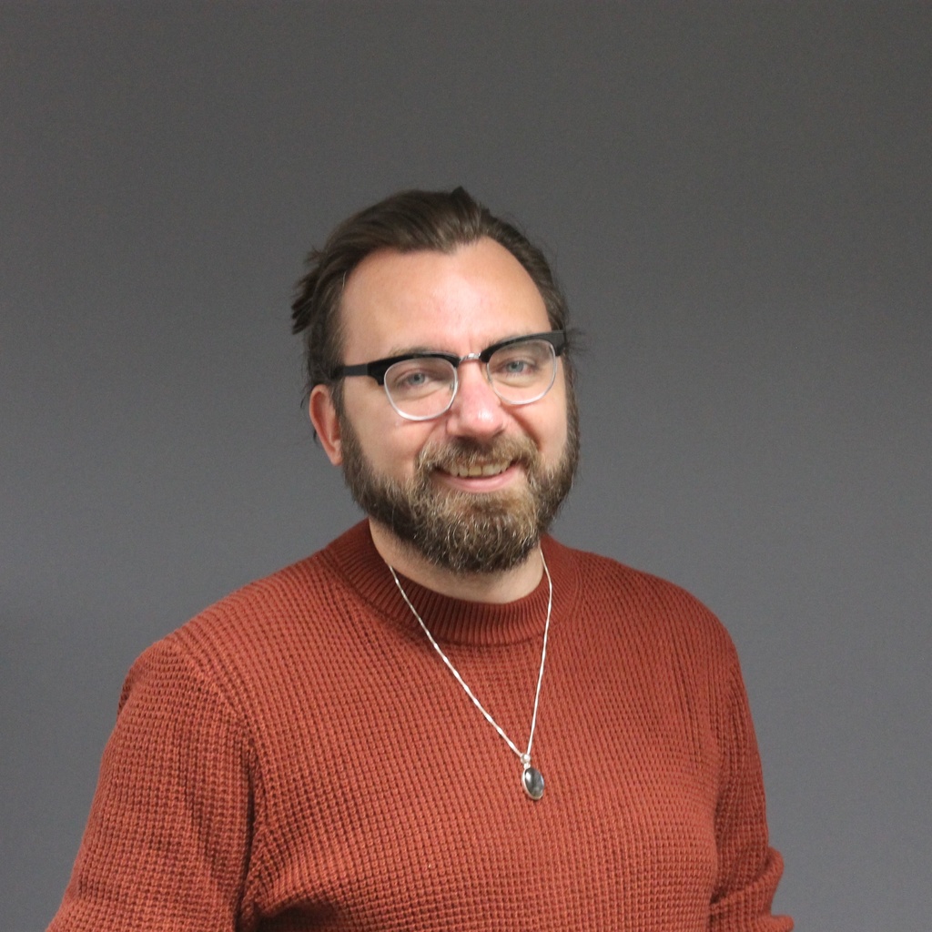 portrait of brown-haired man in rust-colored sweater wearing glasses